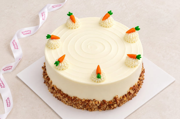 Yummy Bakes Carrot Cake with cream cheese frosting, piped rosettes, carrot decorations and a crushed nut base